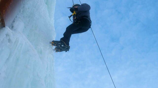 Alpinist man with ice tools axe climbing large wall of ice. going down in rope