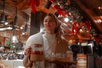 Happy woman holding warm drinklook at the new year tree posing against the festive decor and lights