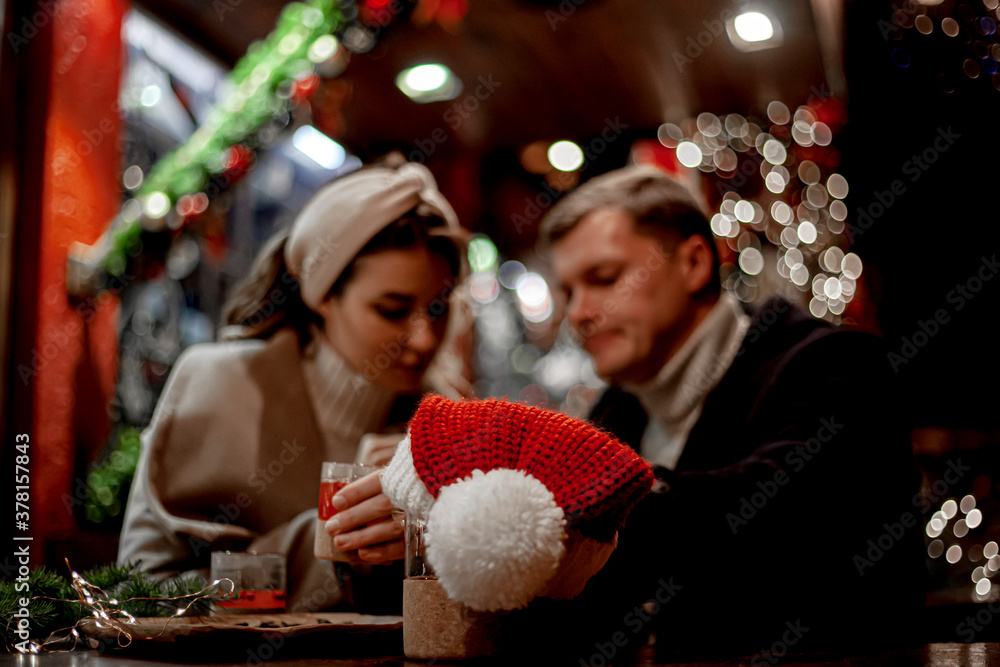 Wall mural Couple in love relationship believe in meracle, kissing against the chrismas decoration outdoor in the eve, look at each other and drink the warm drinks