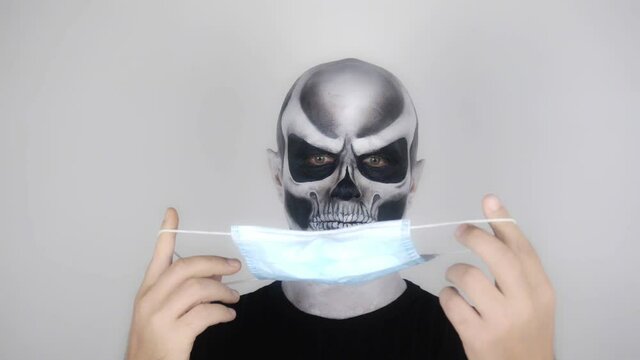 Man in horrible halloween skeleton makeup looks at medical mask in surprise. Covid19. Coronavirus