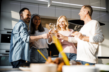 Smiling adult friends cheering with wine at home