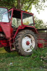 Fototapeta premium Old small red agriculture tractor parked on the grass summertime before sunset three-quarter view
