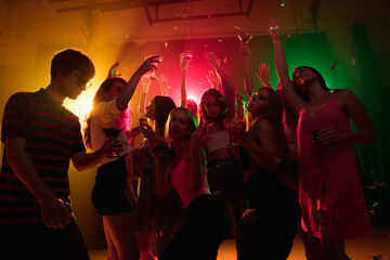 Cocktail. A crowd of people in silhouette raises their hands, dancing on dancefloor on neon light background. Night life, club, music, dance, motion, youth. Bright colors and moving girls and boys.