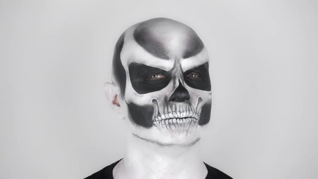 Man in horrible Halloween skeleton makeup posing for the camera. Shooting in the studio. Gray background