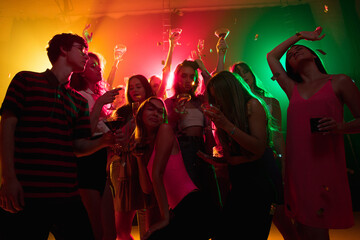 Cocktail. A crowd of people in silhouette raises their hands, dancing on dancefloor on neon light...