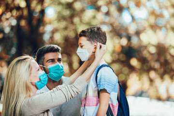 Mother puts a safety mask on her son's face. Schoolboy is ready go to school.