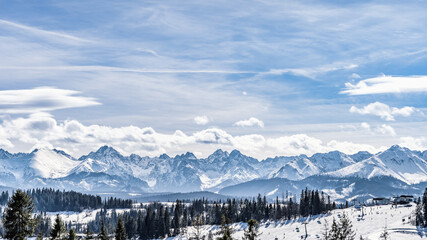 Panoramic view on snowy forest and Tatra Mountains in winter time. Ski slopes and ski lifts in...