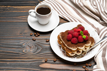portion of Classic tiramisu dessert with raspberries and cup of espresso coffee isolated on wooden background