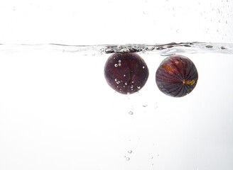 Fresh figs falling deeply into clear water isolated on a white background. Healthy food diet...