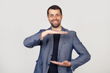 Young businessman man with a beard in a jacket, gesturing with his hands showing a large and large...