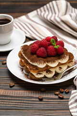 portion of Classic tiramisu dessert with raspberries and cup of espresso coffee isolated on wooden background