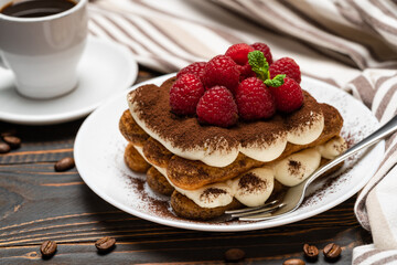 portion of Classic tiramisu dessert with raspberries and cup of espresso coffee isolated on wooden background