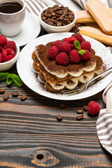portion of Classic tiramisu dessert with raspberries, savoiardi cookies and cup of espresso coffee isolated on wooden background