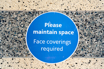 Circular sign on floor enforcing social distancing and face coverings