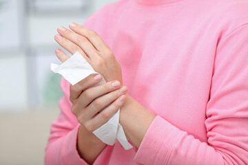 Woman cleaning hands with paper tissue on blurred background, closeup