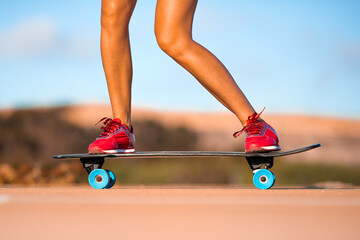 Close up photo of cool young fit woman with beautiful legs in red sneakers riding skateboard in shiny summer day . Outdoor activities. Street culture.