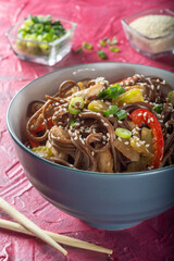 Wok with soba noodles. Buckwheat soba noodles in a grey Cup with chopsticks. Soba noodles with chicken, celery and red sweet pepper.