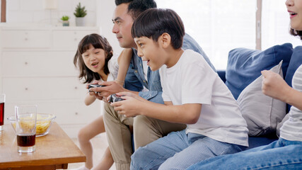 Candid of happy asian family play video game at home feeling excited fun holding console in hand in quarantine activity, entertainment at home concept. Competition and funny in leisure time or hobby.