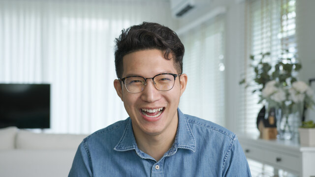 Portrait or headshot of young adult asian handsome man or model wearing eye glasses with cool hair big smiling confident and looking to camera with feeling happy and positive in living room at home.