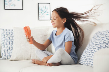Little girl enjoying air flow from portable fan at home. Summer heat - obrazy, fototapety, plakaty