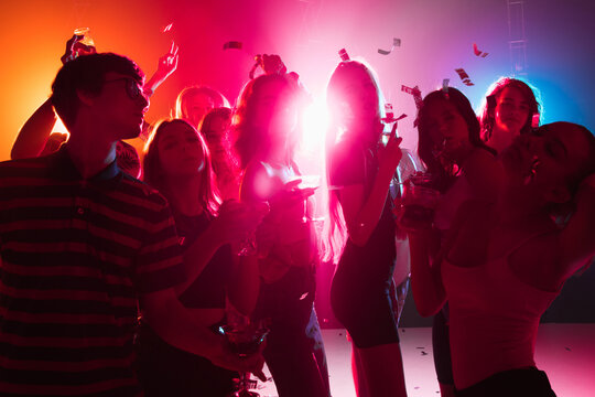 Wild. A Crowd Of People In Silhouette Raises Their Hands, Dancing On Dancefloor On Neon Light Background. Night Life, Club, Music, Dance, Motion, Youth. Bright Colors And Moving Girls And Boys.