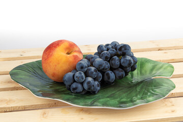 a fresh peach and a bunch of grapes on a green leaf shaped plate on a white background