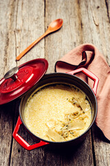 Creamy Polenta with baked onion and cheese in cast iron pot on rustic wooden background. Italian food. Selective focus. Toned image