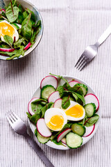 Radish, cucumber, herb mix and soft-boiled egg salad in two bowls on white tablecloth. Healthy nutrition. Selective focus