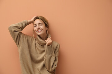 Beautiful young woman wearing knitted sweater on light brown background. Space for text
