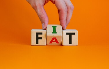 Hand turns a cube and changes the word fat to fit. Beautiful orange background. Lifestyle and healthy concept. Copy space.