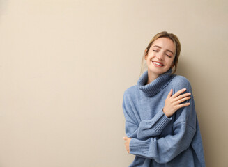 Beautiful young woman wearing knitted sweater on beige background. Space for text