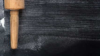 Rolling Pin on textured black bord  with traces Wheat Flour. Free space for text.