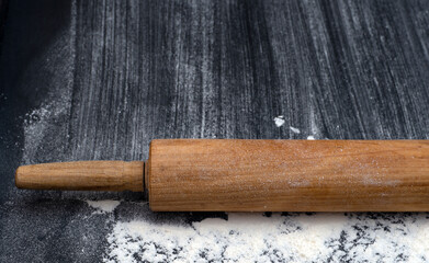Rolling pin  on textured black bord  with traces Wheat Flour. Free space for text 