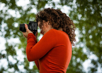 A curly Caucasian woman holding a camera during an outdoors shooting
