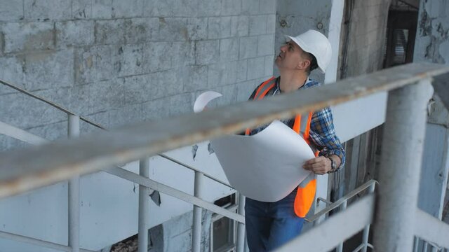 Worker with construction documentation at project site. Master builder in hard hat with design drawings at construction site