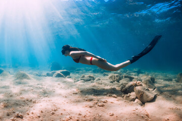 Obraz na płótnie Canvas Freediver woman in bikini glides in blue sea and sun rays. Freediving with fins underwater in ocean