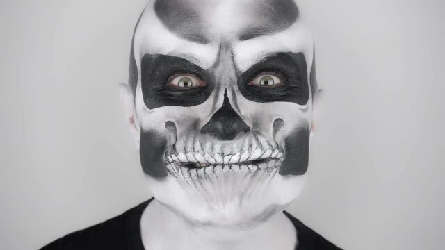 Man in horrible halloween skeleton makeup trying to scare. Shooting in the studio. Gray background