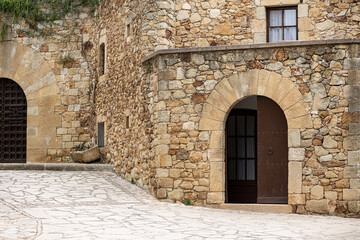 Fototapeta na wymiar Arc entry facade door on a medieval rock stone building with cobble stones street
