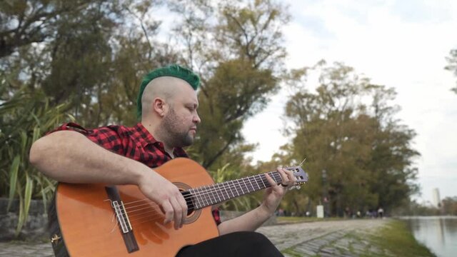 Slow motion of an alternative man playing guitar at park. Copy space at right, dolly in