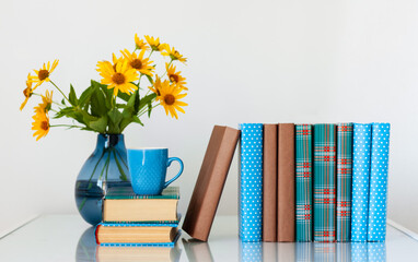 Cozy home interior decor: stack of books and vase with yellow flowers on a table. Distance home education.Quarantine concept of stay home.
