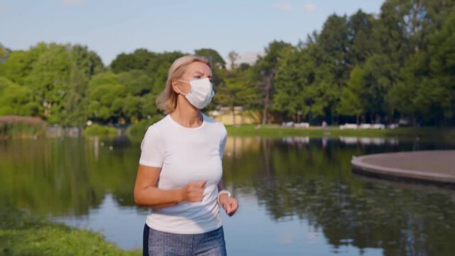 Senior sporty woman wearing safety mask jogging in summer park