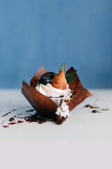 The cake with a fruit filling is decorated with a creamy white flower. Top decorated with chocolate chip cookies and blueberries. The composition ends with green leaves. Packed in a paper cup standing