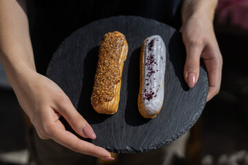 Raspberry and caramel eclair on round black rock stand in hands. Two eclairs with white and brown...