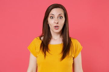 Shocked amazed surprised young brunette woman 20s wearing yellow casual t-shirt posing standing keeping mouth open saying wow looking camera isolated on pink color wall background studio portrait.