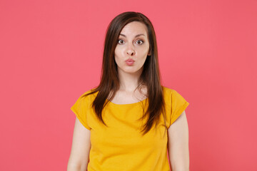 Fototapeta premium Pretty amazed beautiful young brunette woman 20s wearing yellow casual t-shirt posing and standing blowing lips cheeks looking camera isolated on pink color wall background studio portrait.