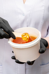 Honey depilation. Natural hair removal. Sugar wax in pot in female specialist hands wearing black...