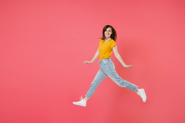 Fototapeta na wymiar Full length side view portrait of smiling young brunette woman 20s wearing yellow casual t-shirt posing jumping spreading hands and legs looking camera isolated on pink color wall background studio.