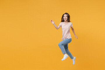 Fototapeta na wymiar Full length portrait of excited cheerful funny young woman 20s wearing pastel pink casual t-shirt posing jumping like running looking aside isolated on bright yellow color wall background studio.