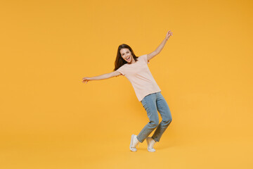 Full length portrait of funny laughing young woman 20s in pastel pink casual t-shirt posing dancing rising spreading hands standing on toes looking camera isolated on yellow color background studio.