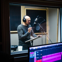 Bald man near microphone recording voice.